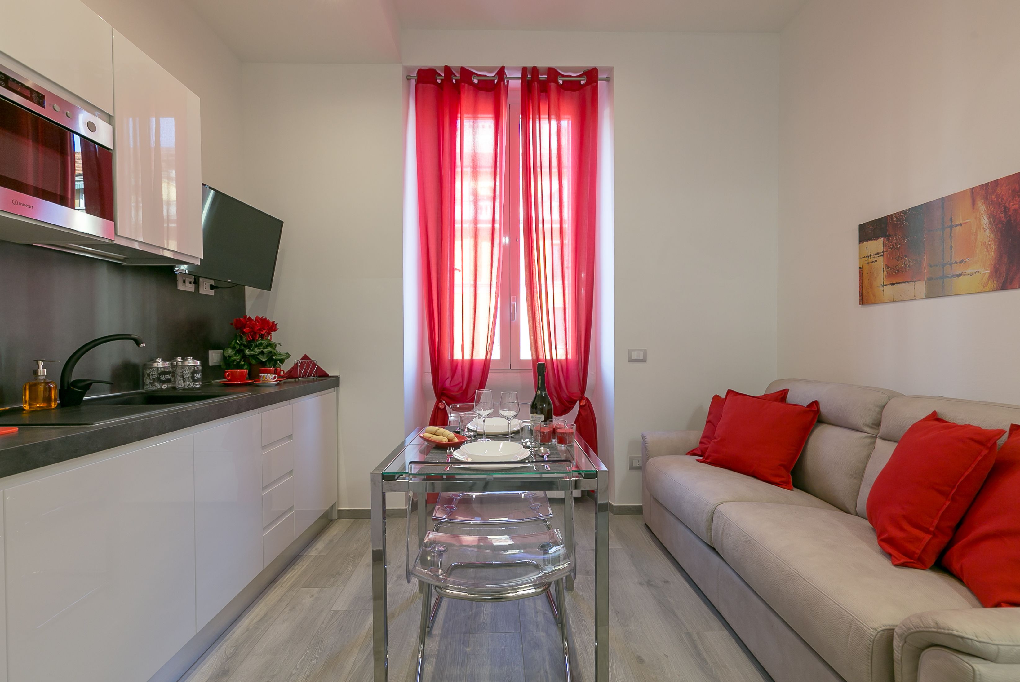 A modern kitchen with white cabinets, a stainless steel range hood, and a glass dining table set with red accents.