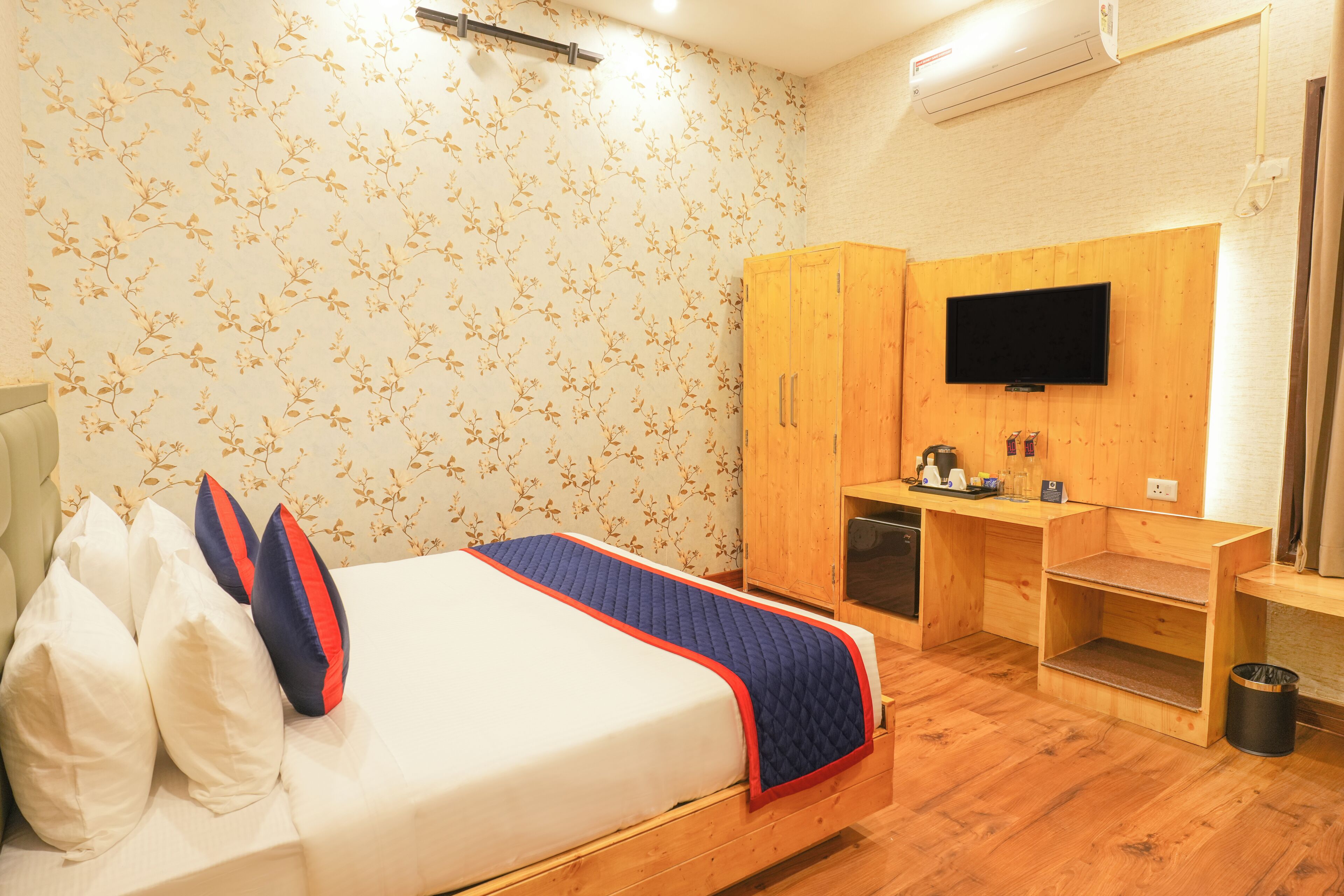 A hotel room with a bed, a wooden desk, a television, and a wardrobe.