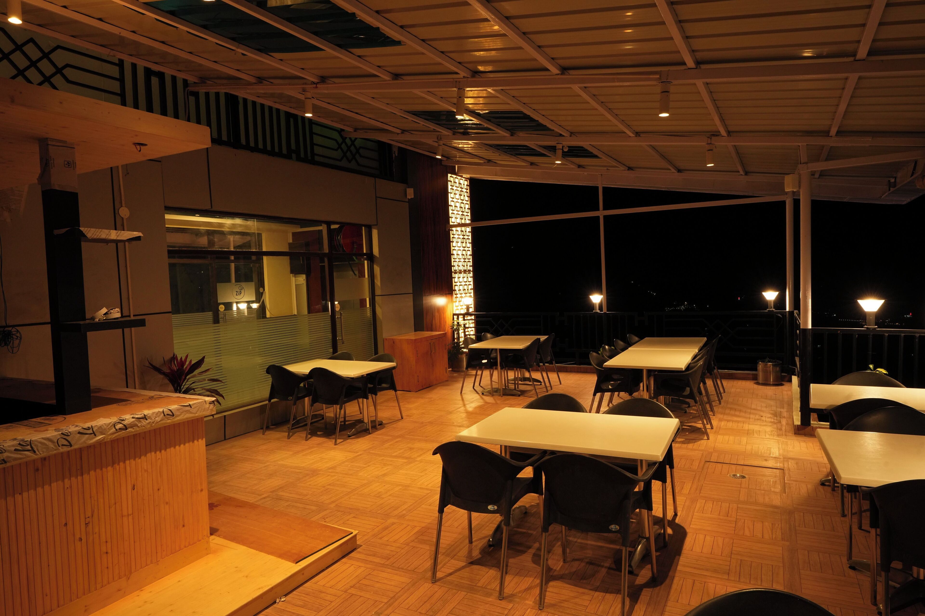 An outdoor dining area with tables and chairs, a counter, and a view of the city at night.