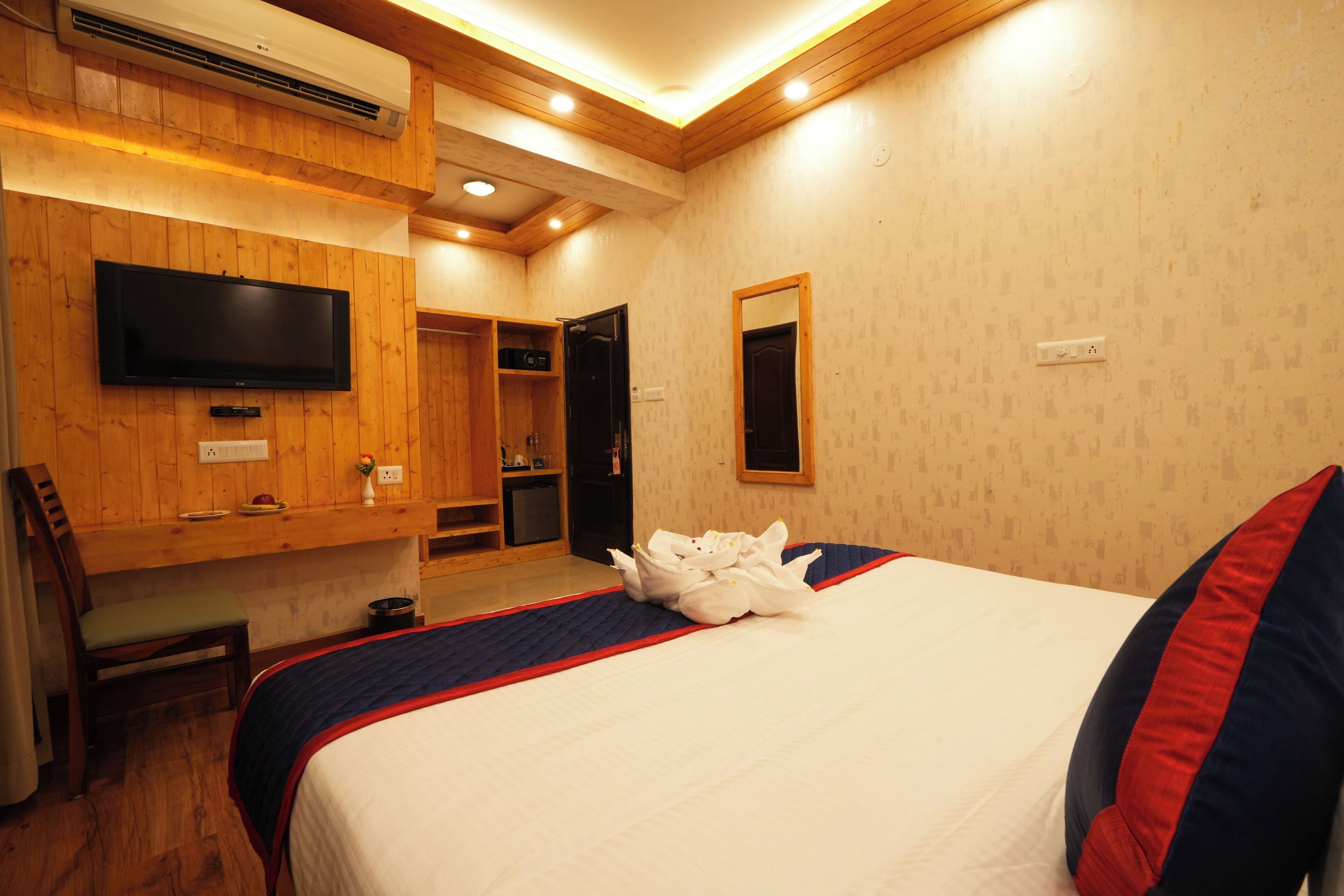 Quarto de hotel com uma cama, televisão fixada na parede, um banco de madeira e um espelho.