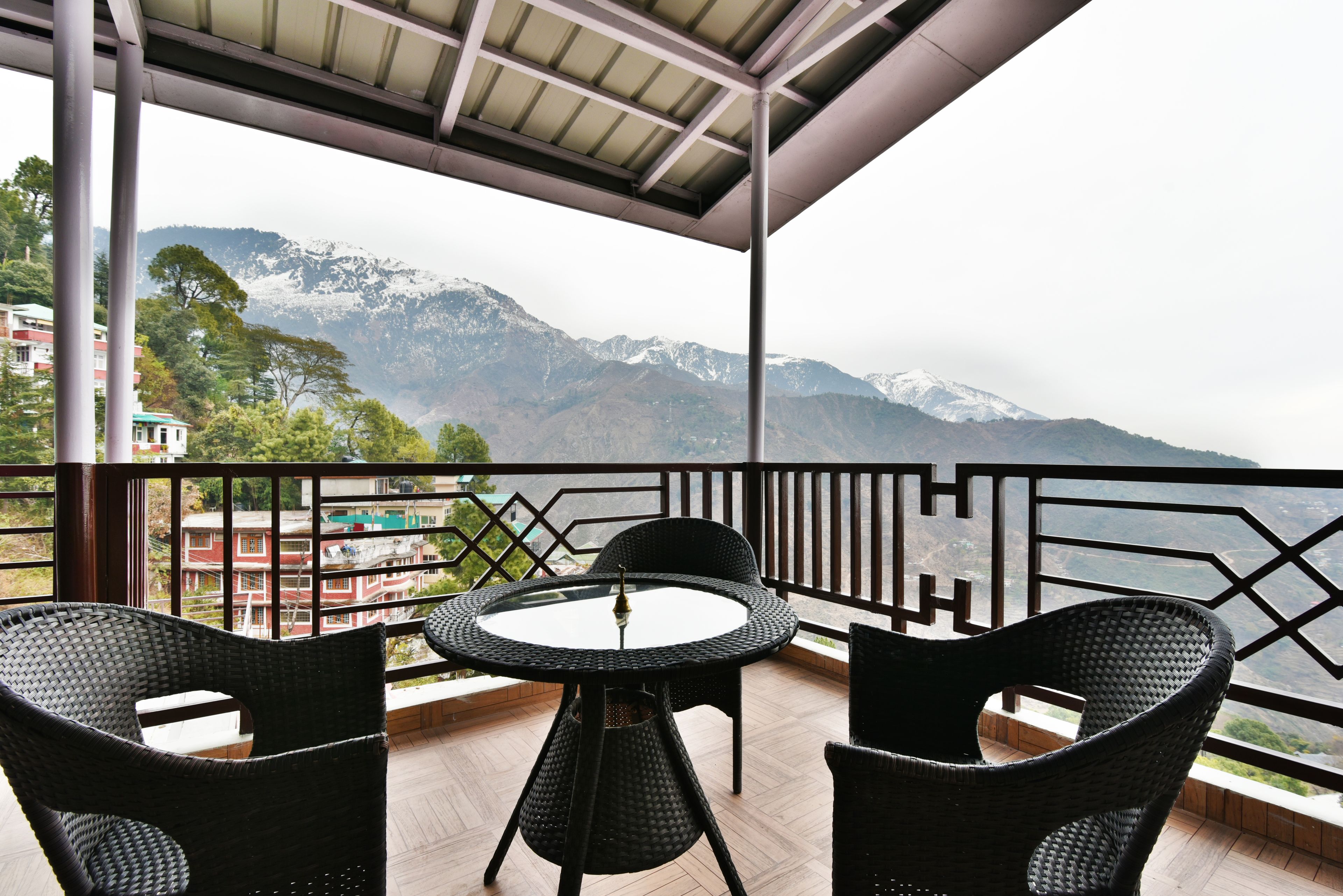 A balcony with wicker chairs and a table, overlooking a mountainous landscape.