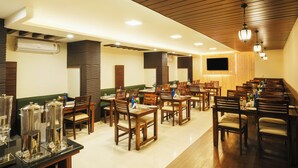 A restaurant with wooden tables and chairs, a flat-screen TV mounted on the wall, and an air conditioning unit on the wall. - Hotel Bella Heights (Dharamshala)