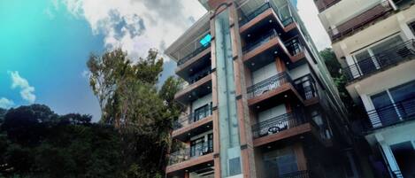 Un hotel de varios pisos con balcones, un cartel que indica 'Zip' y 'Bella Weights' en la fachada, y un cielo despejado con luz solar.