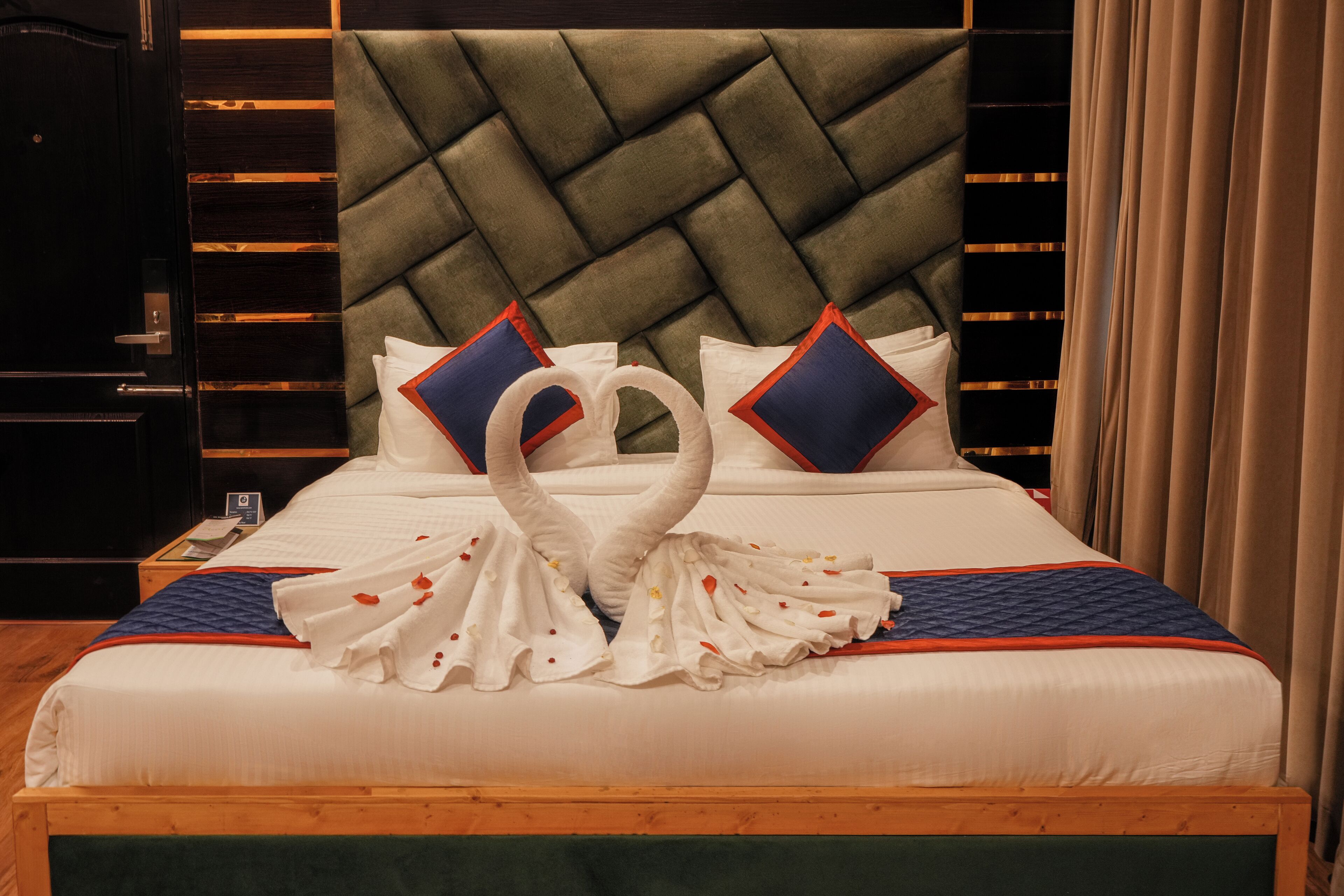 Una cama bien hecha con un arreglo de toallas en forma de cisne, un cabecero tapizado y un marco de madera.