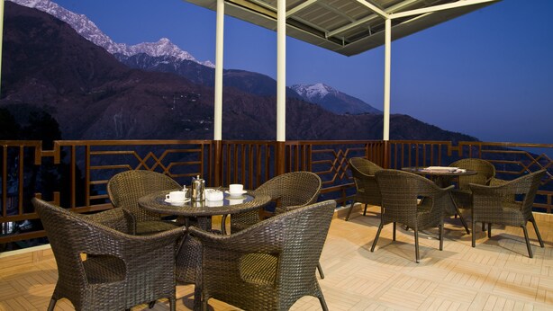 An outdoor seating area with wicker furniture and a view of snow-capped mountains. - Hotel Bella Heights (Dharamshala)