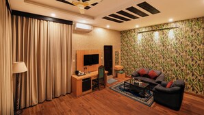 A modern living room with a wooden desk, a flat-screen TV, a sofa, and a patterned wallpaper. - Hotel Bella Heights (Dharamshala)