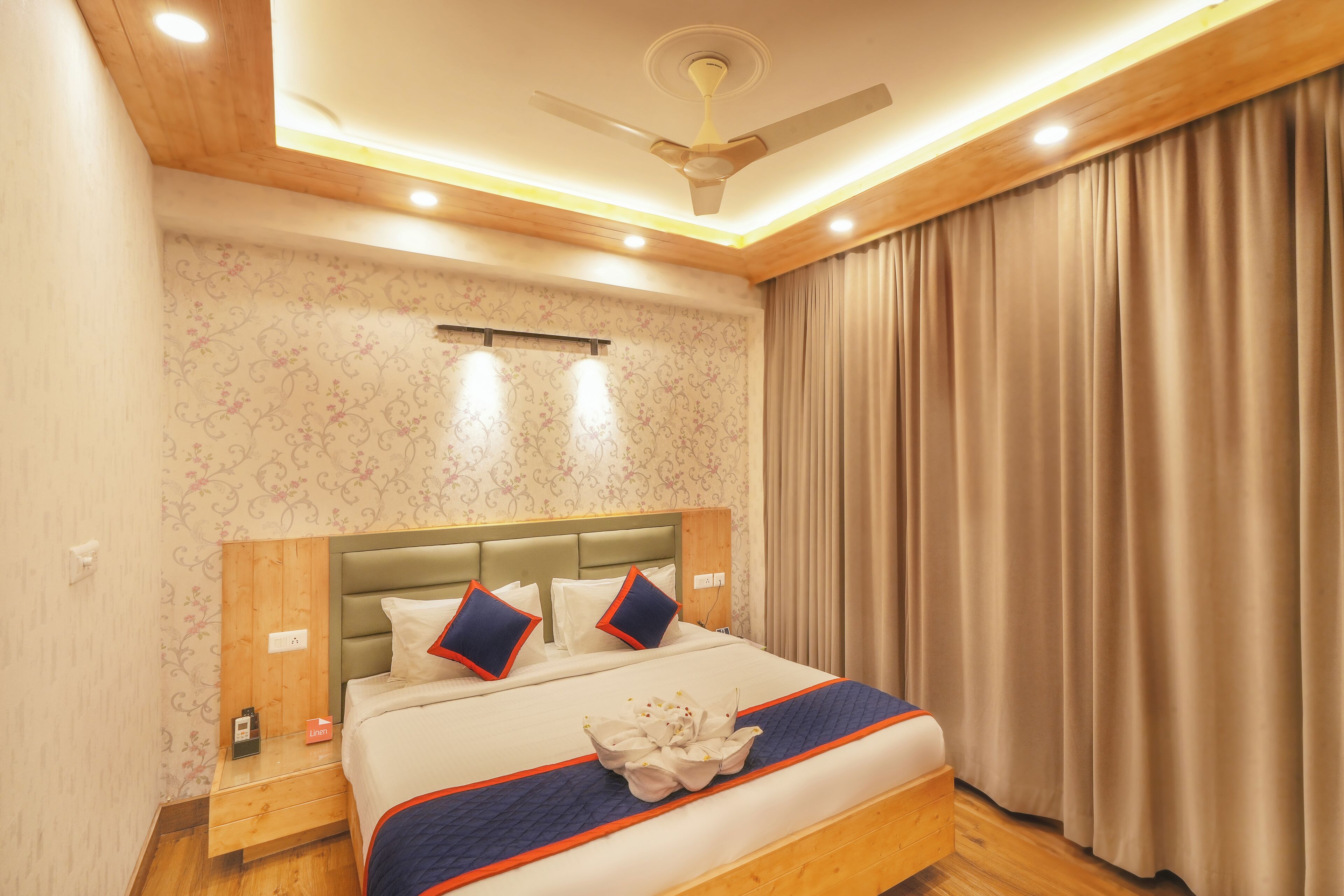 Ein Hotelzimmer mit einem Bett, einem Holz-Kopfteil, Vorhängen und einem Deckenventilator.