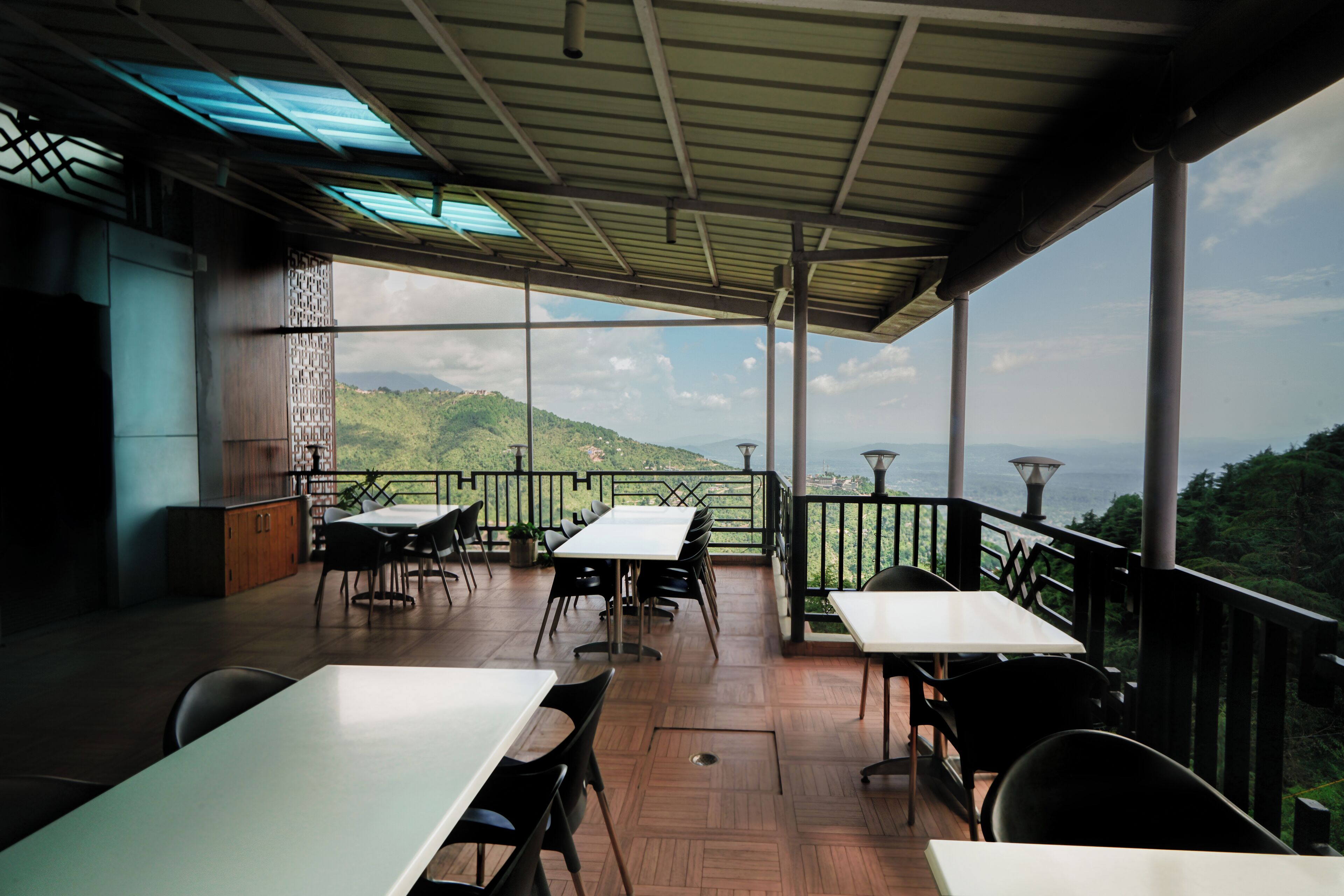 Un espacio de comedor al aire libre techado con mesas y sillas, con vistas a un paisaje montañoso.