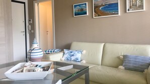 Ein Wohnzimmer mit einem beigefarbenen Sofa, einem Glastisch und drei Bildern an der Wand.