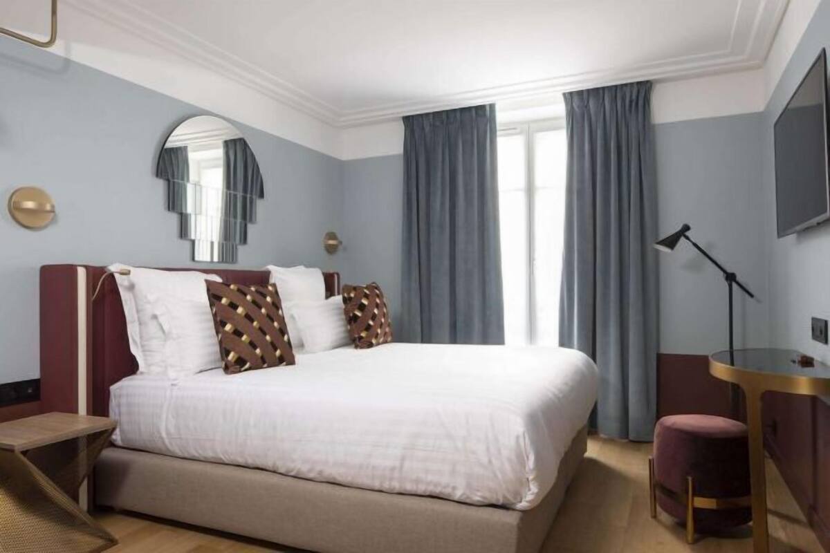 A hotel room with a large bed, a desk, a chair, a TV, and a window with curtains.