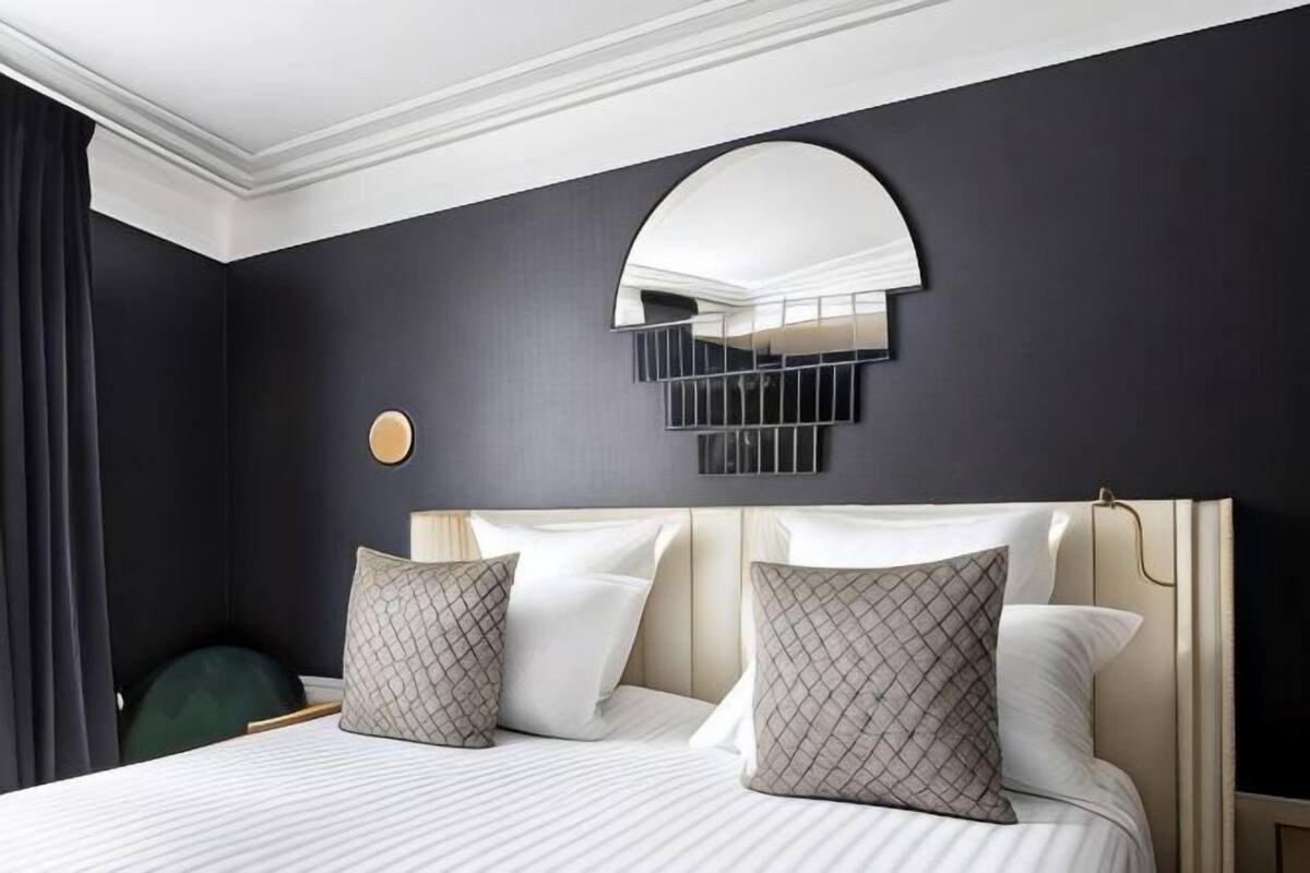 A hotel room with a large bed, a curved mirror, and a dark wall.
