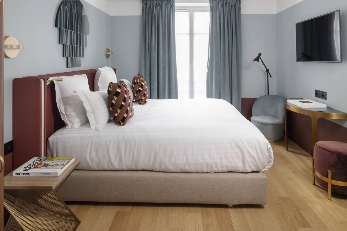 A modern hotel room with a large bed, a desk, a chair, and a TV.
