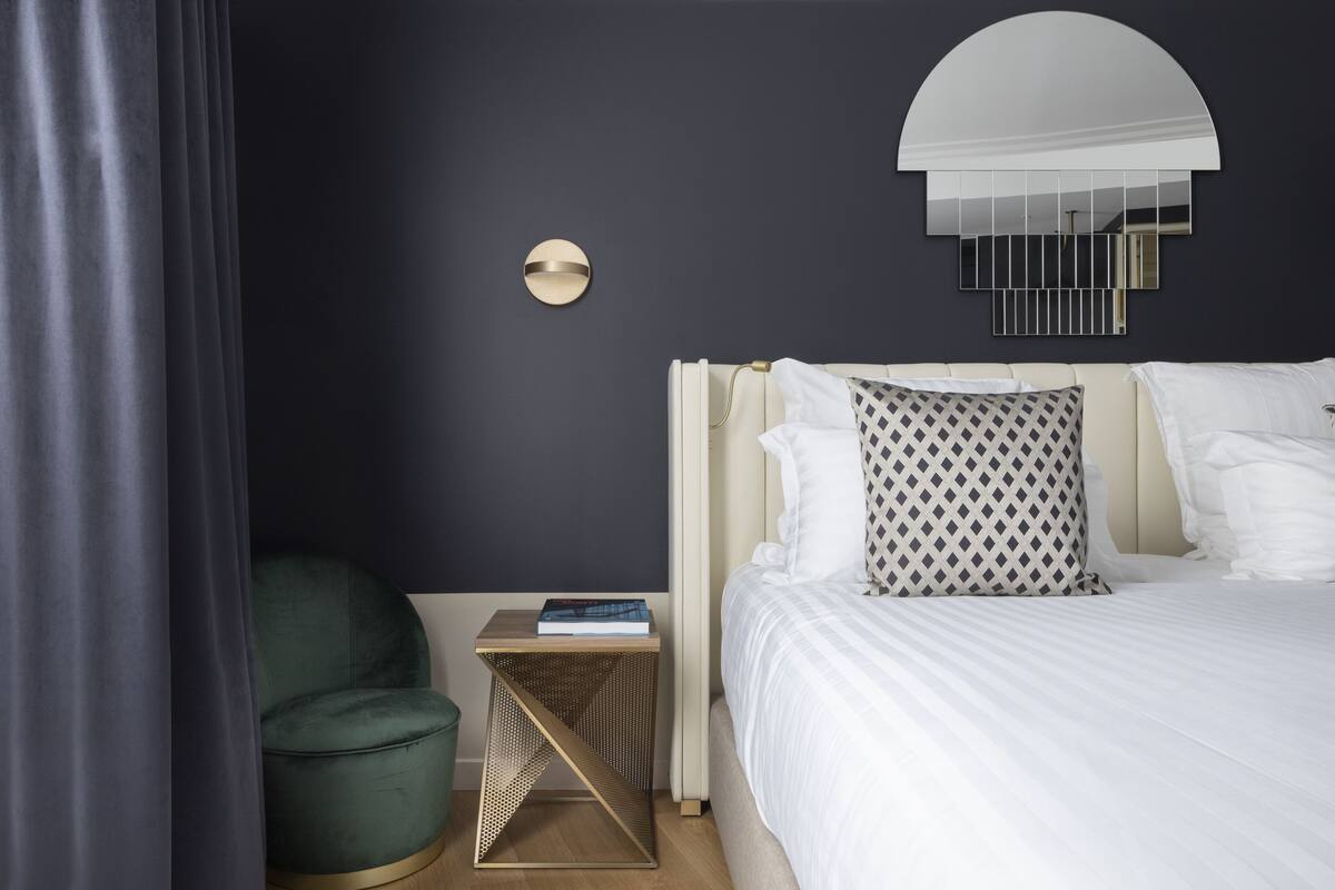 A modern bedroom with a bed, a bedside table, a green chair, and a wall-mounted mirror.