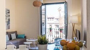 Een gezellige zithoek met een bank, een tafeltje met een plant en een balkon met uitzicht op gebouwen.