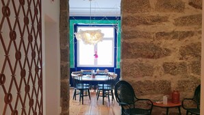 A dining area with a round table and chairs, a stone wall, and a decorative hanging light fixture. - Supernova - Hostel (Porto)