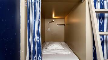 Habitación pequeña con cama individual, cortina, luz en la pared y toma de corriente.