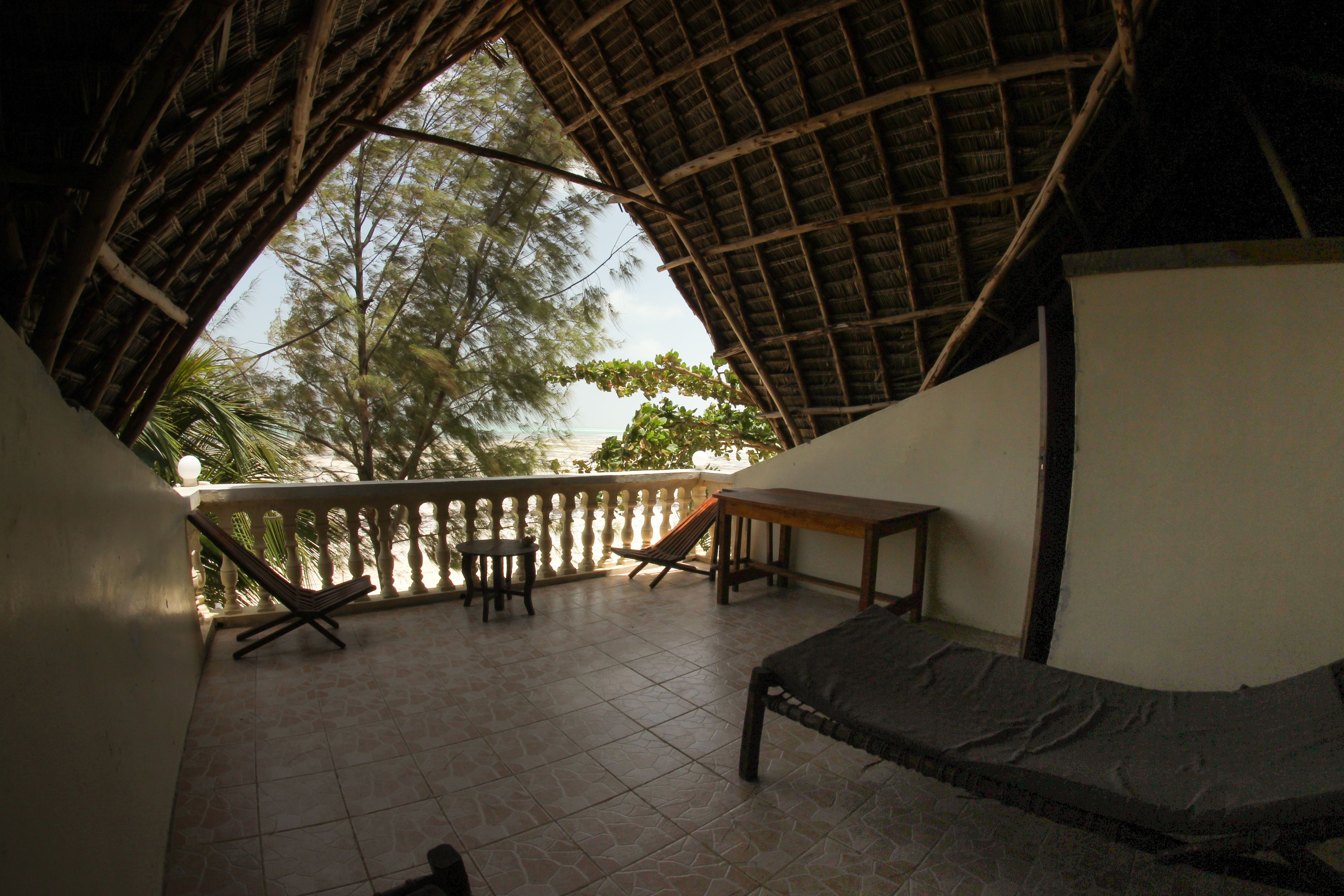 A room with a thatched roof, a bed, a table, and a chair.
