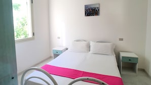 A bedroom with a bed, two bedside tables, a nightstand, a window, and a painting on the wall. - Appartamento Robinia (Gallipoli)