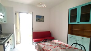 A compact kitchen with a stove, sink, and cabinets. There is a dining table with chairs and a red sofa in the living area. - Appartamento Robinia (Gallipoli)