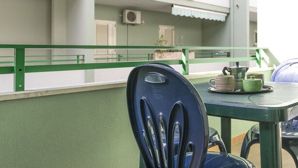 A balcony with a green railing, a table with a chair, and a tray with tea set. - Appartamento Robinia II (Gallipoli)