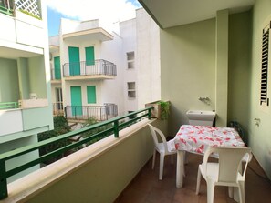 A balcony with a table and chairs, a hanging plant, and a view of neighboring buildings. - Appartamento Robinia II (Gallipoli)