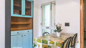 A room with a teal cabinet, a white door with frosted glass, a table with a colorful tablecloth, and a potted plant. - Appartamento Robinia II (Gallipoli)
