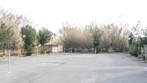 A gated parking area with a gravel surface, surrounded by tall grasses and trees. - Appartamento Robinia II (Gallipoli)