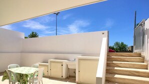 Eine Außenpatio-Terrasse mit Tisch, Stühlen, einer kleinen Küchenzeile und einer Treppe zu einer erhöhten Ebene.