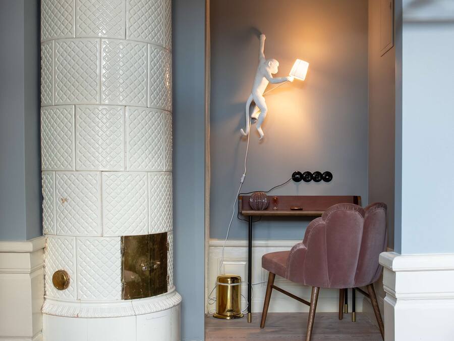 A room with a white textured column, a pink chair, a small table with a lamp, and a wall-mounted light fixture.