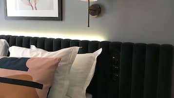 Una cama bien hecha con almohadas, una mesita redonda, una lámpara de pared y una obra de arte enmarcada en la pared.