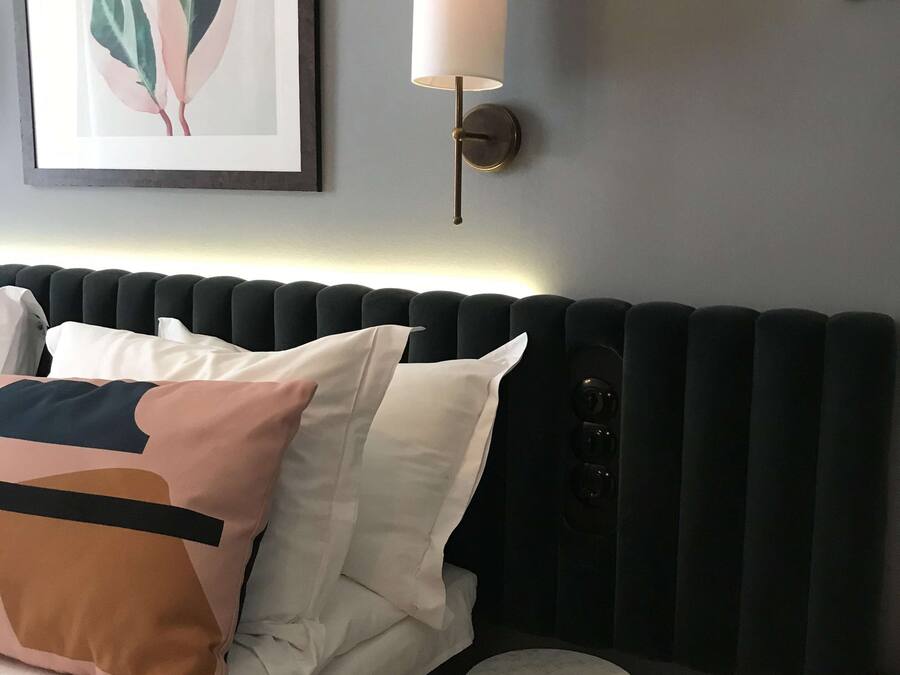 Una cama bien hecha con almohadas, una mesita redonda, una lámpara de pared y una obra de arte enmarcada en la pared.