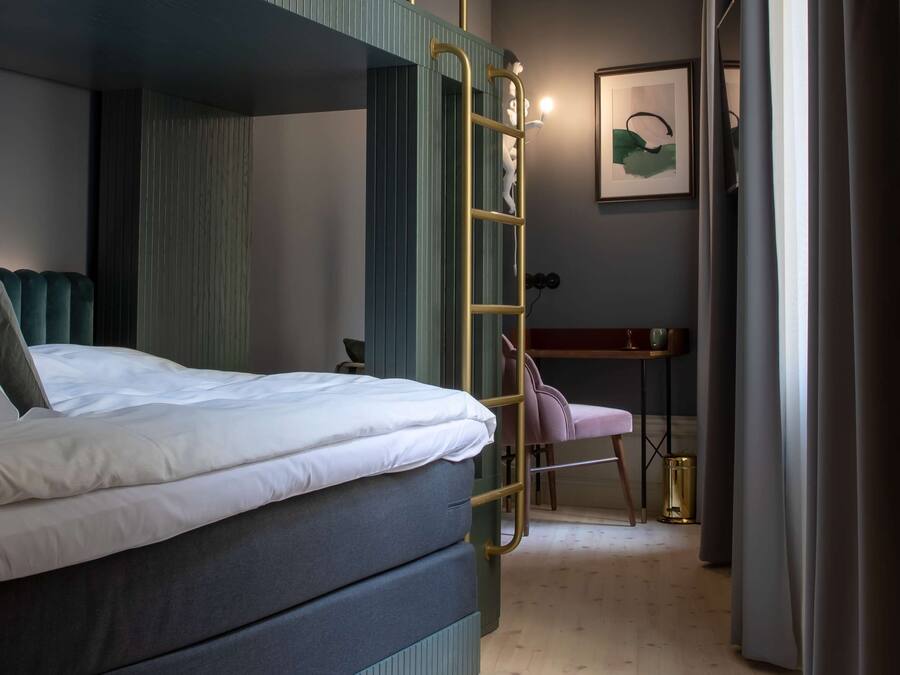 A bunk bed with a ladder, a desk, and a chair in a room with wooden flooring.