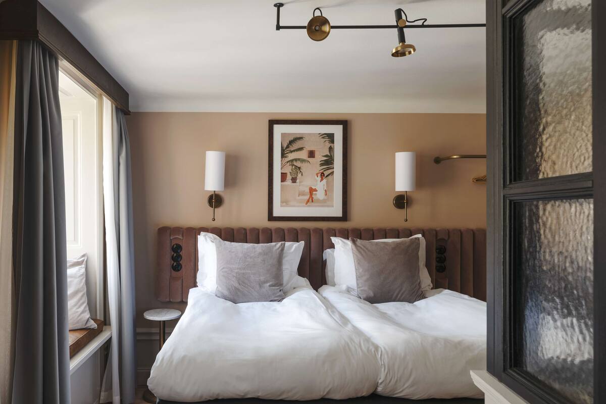 Habitación de hotel con una cama grande, dos mesitas de noche, una pequeña mesa redonda y un cuadro en la pared.