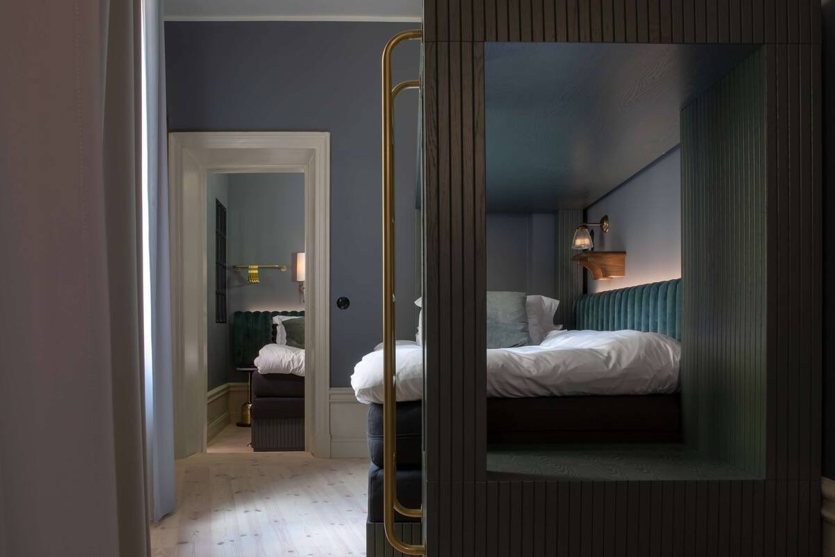 Una habitación de hotel moderna con un espejo grande, una cama, una mesita de noche y una lámpara.
