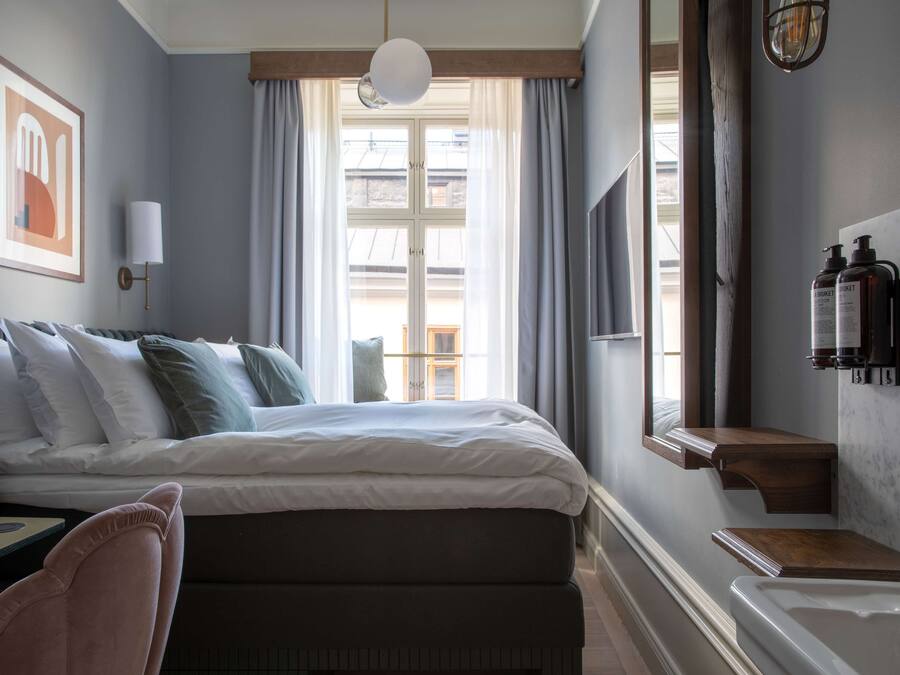 Ein Schlafzimmer mit Bett, Nachttisch, Lampe und einem Fenster mit Vorhängen.