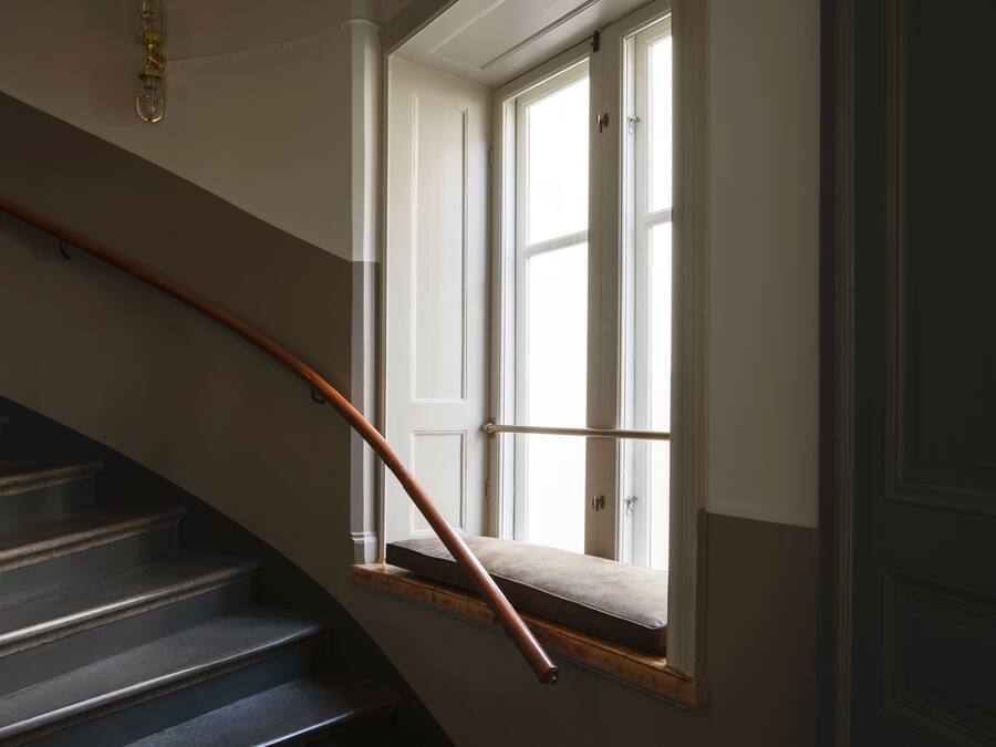 A staircase with a wooden handrail leading to a landing with a window.