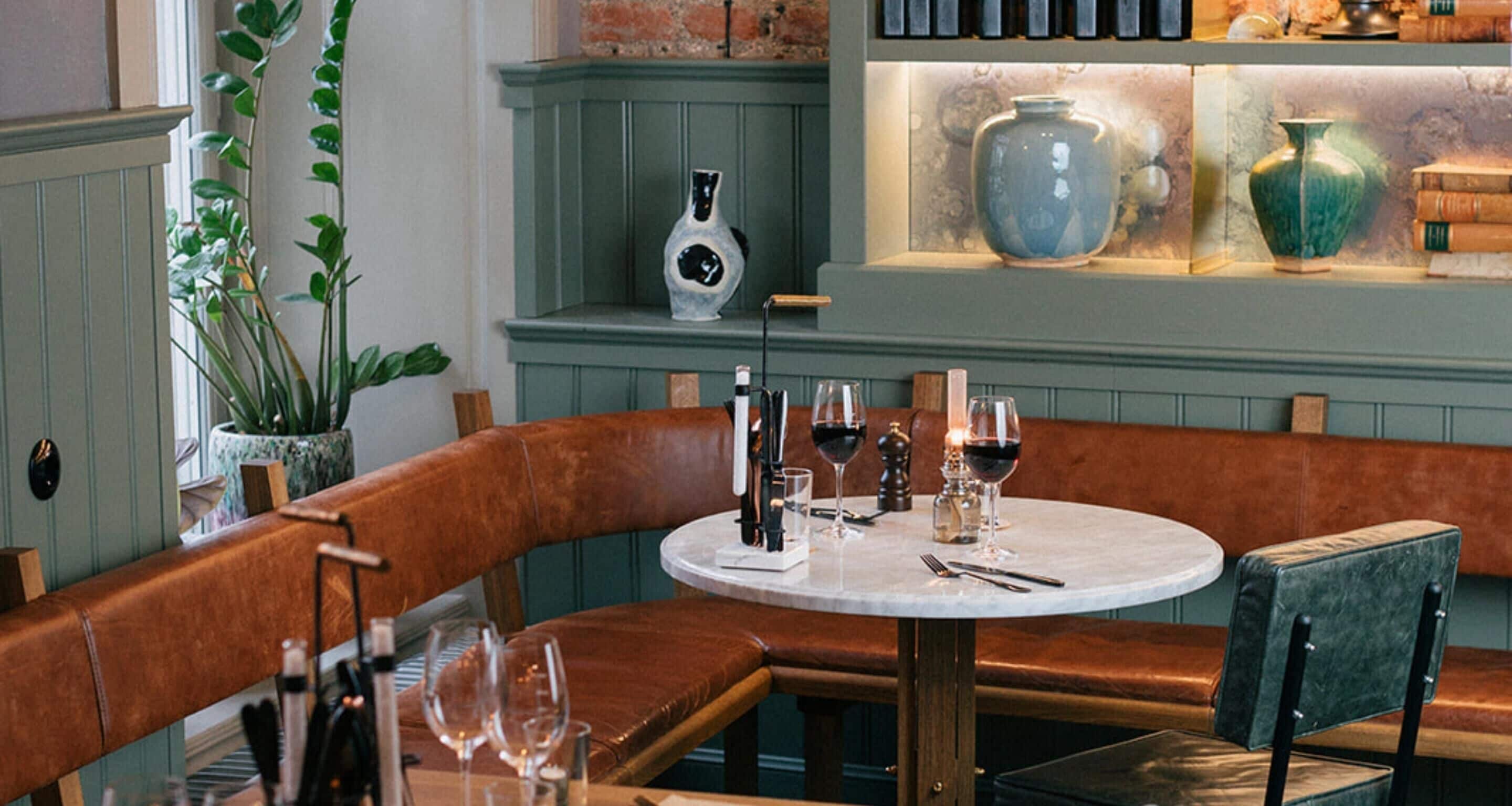 A restaurant interior with a round table, leather seating, and decorative vases on shelves.