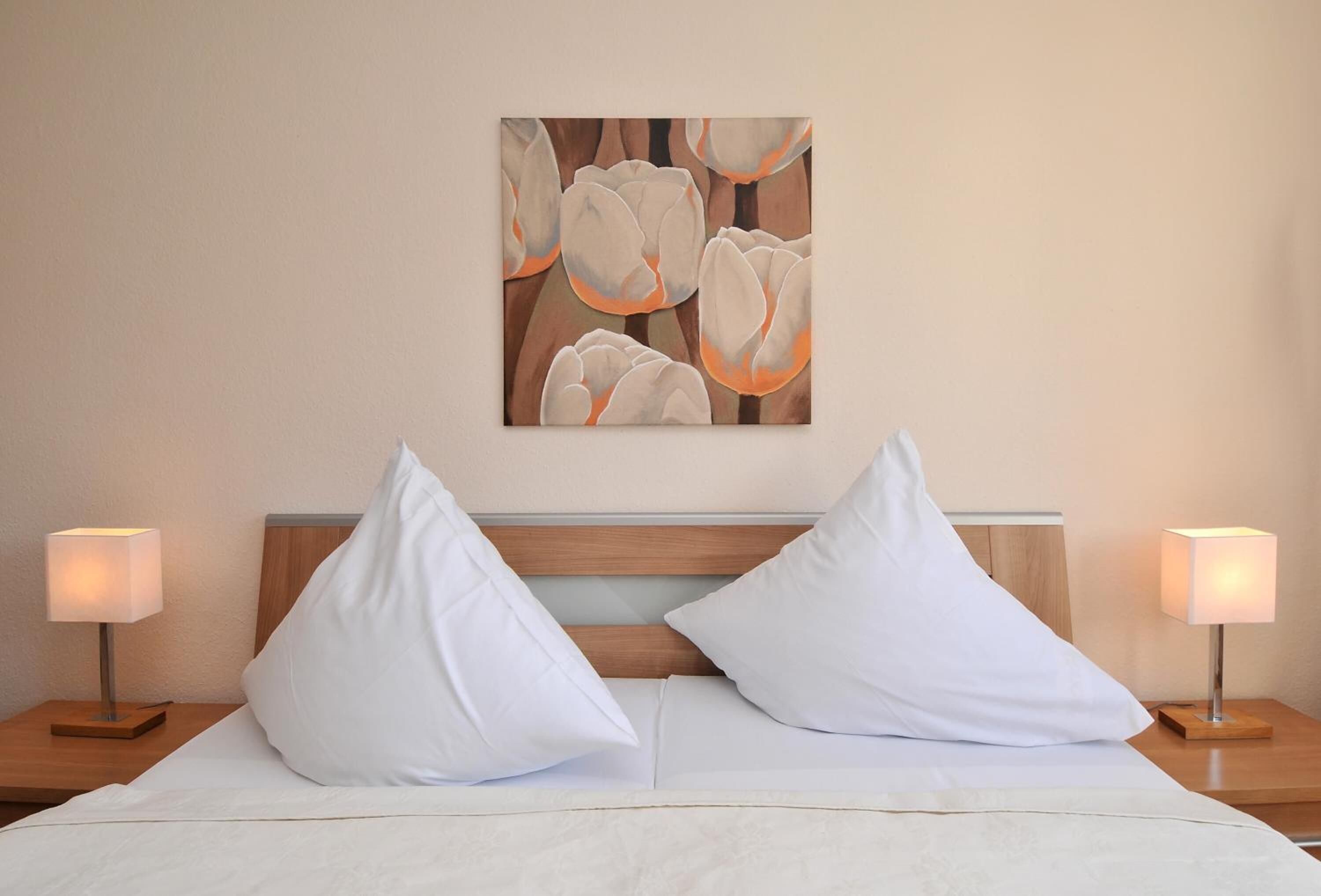 A hotel room with a bed, two bedside lamps, and a painting on the wall.