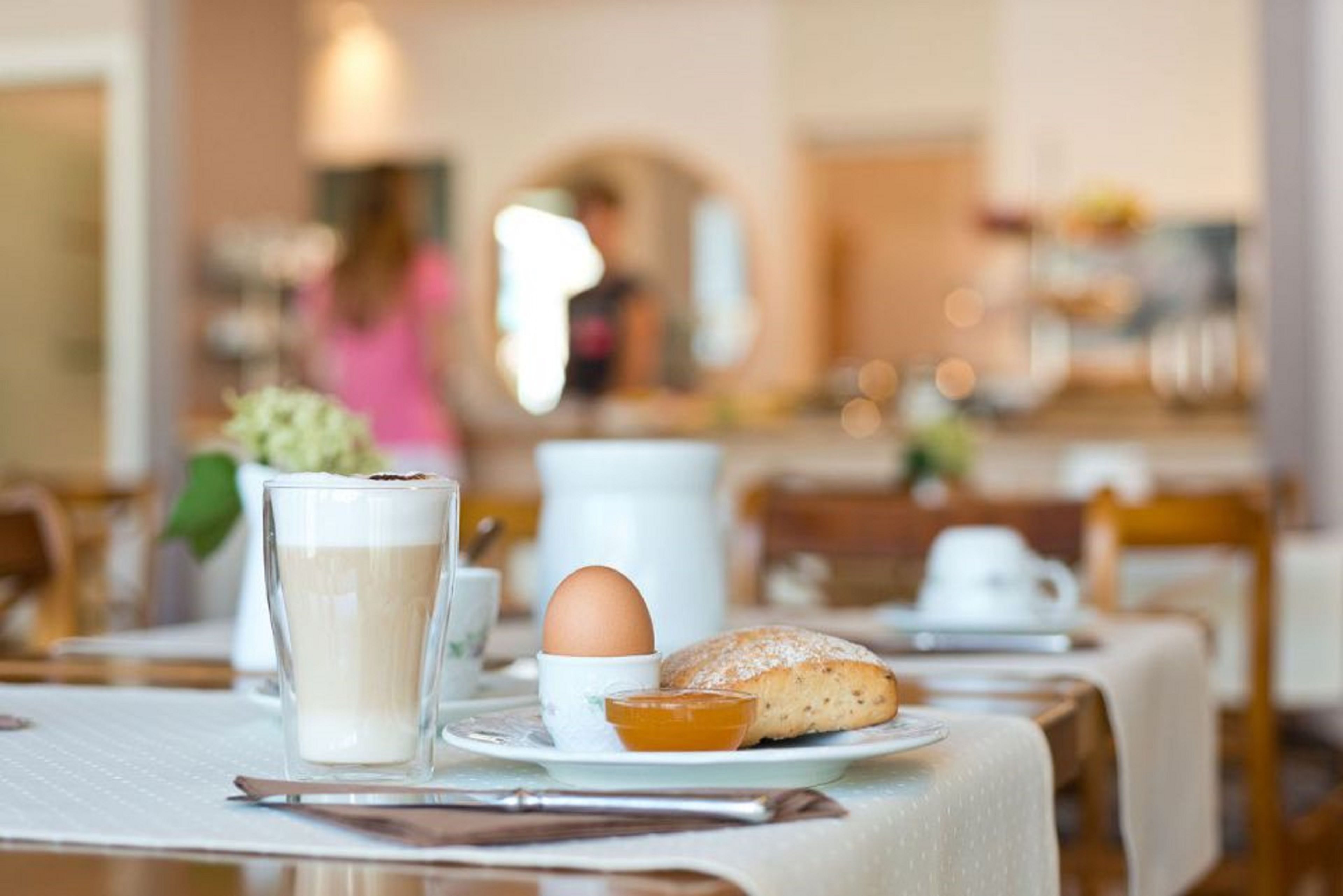 Un desayuno con un vaso de leche, un croissant, un pastel y una taza de café sobre una mesa.