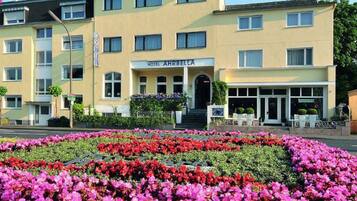 Hotel Ahrebel-la features a symmetrical facade with a central entrance and windows, surrounded by a well-maintained garden.