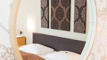 A bedroom with a round mirror reflecting a bed, a nightstand, and patterned wallpaper.