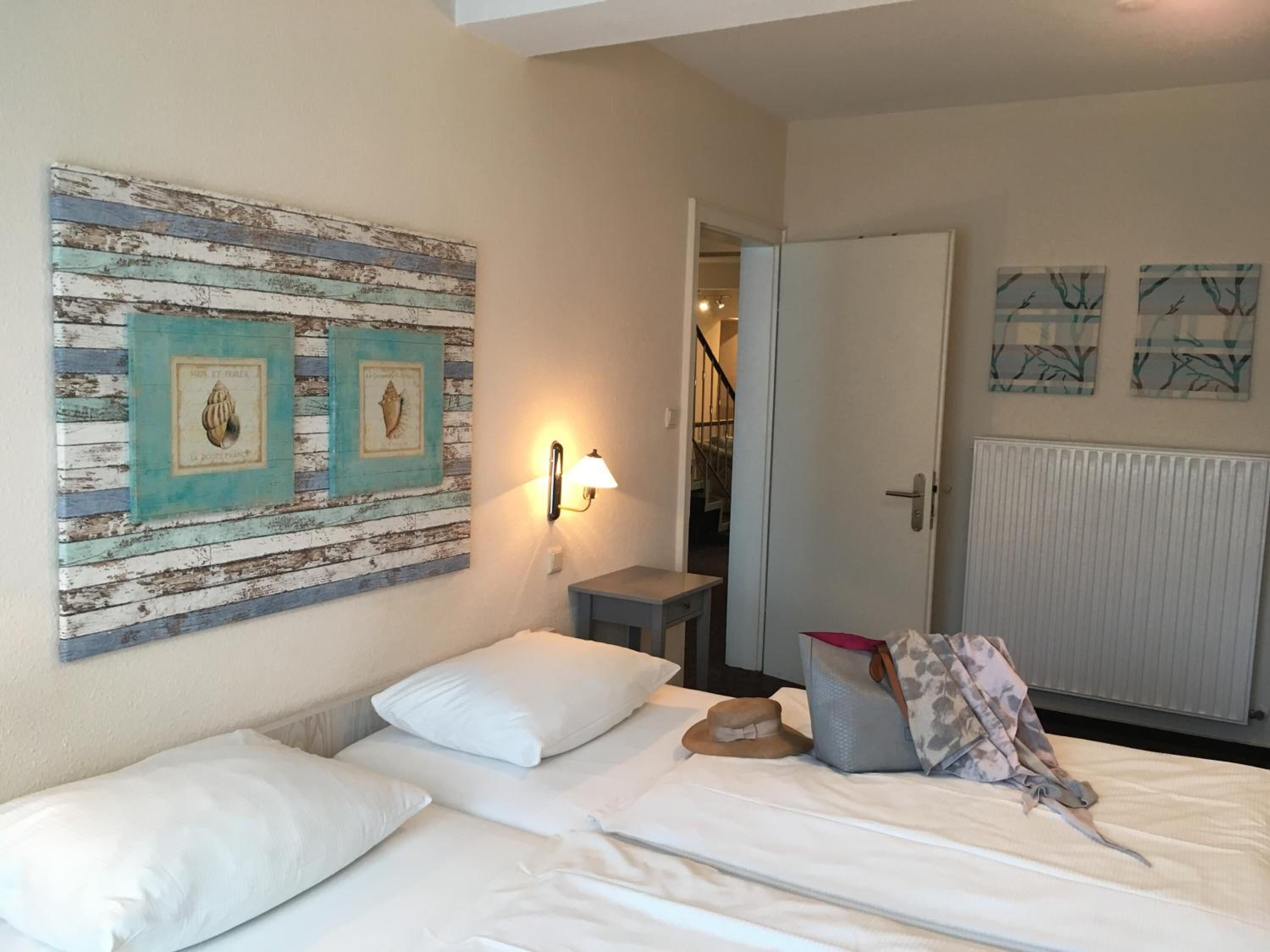 Une chambre d’hôtel comprenant un lit, une table de chevet, une lampe fixée au mur et des œuvres d’art.