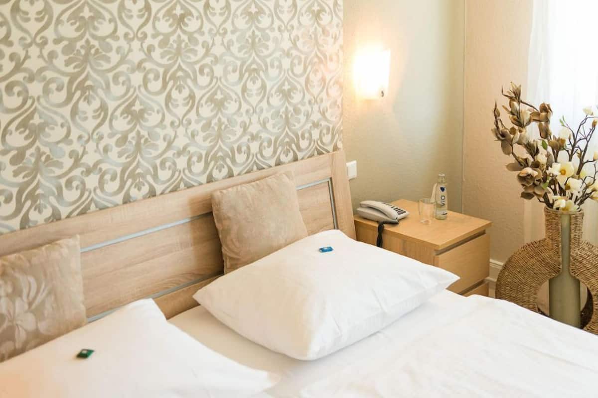 A hotel room with a bed, bedside table, lamp, and a decorative vase.