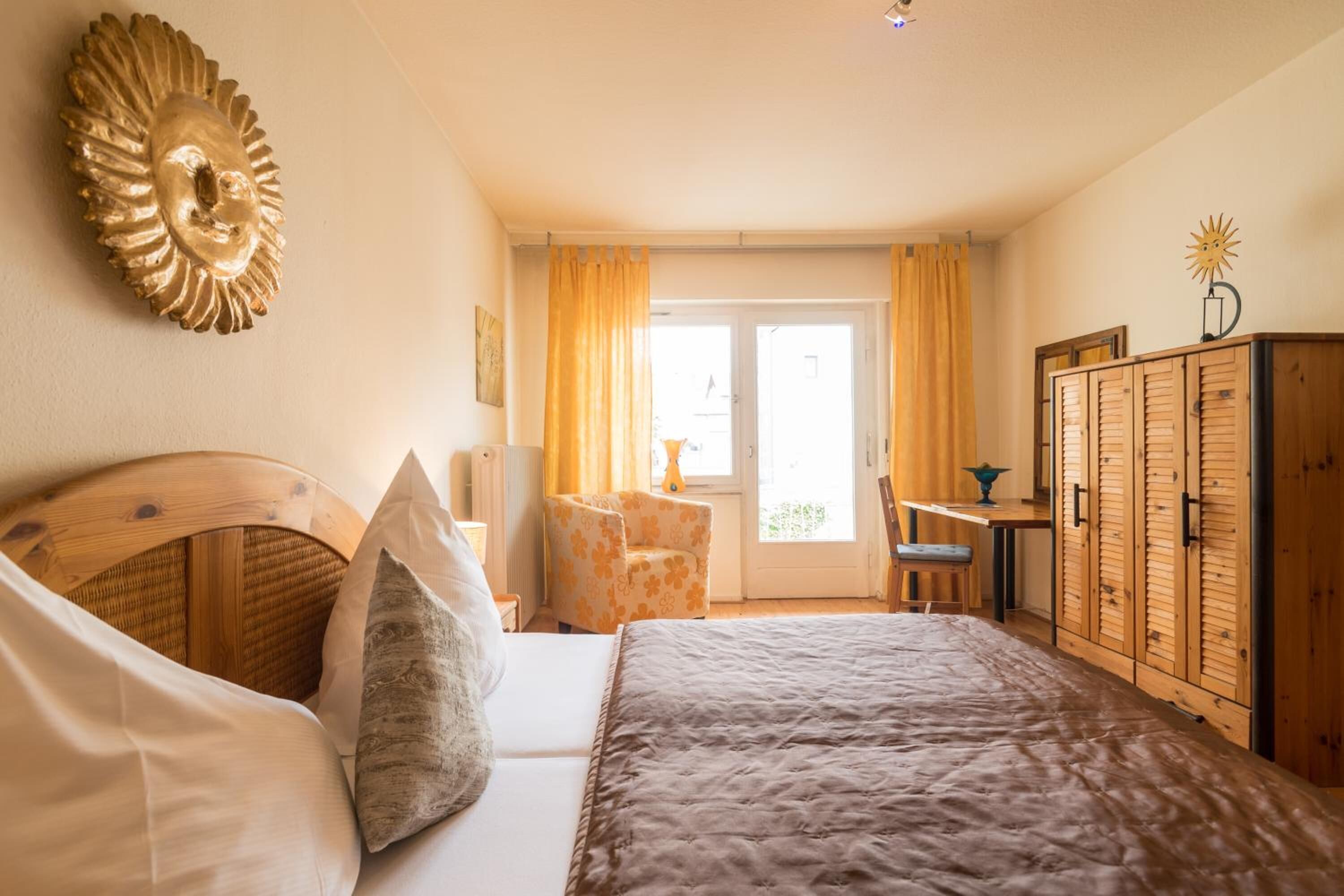 A bedroom with a bed, a wooden wardrobe, a chair, and a desk.