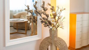 A room with a mirror reflecting a dining area, a wicker vase with branches and flowers, and a white cabinet with drawers. - Hotel Ahrbella (Bad Neuenahr-Ahrweiler)