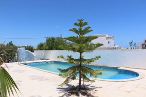 Relax by the serene pool surrounded by a palm tree and a pebble-lined border.