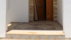 Un bâtiment blanc avec une porte en bois et un porche dallé de pierres.