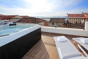 A rooftop terrace with a hot tub, lounge chairs, and a view of buildings and mountains. - Villa Vito (Bibinje)