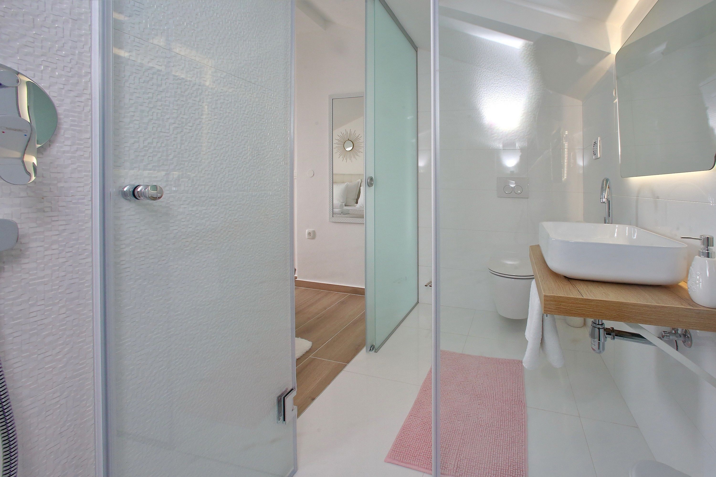 A modern bathroom with a glass shower enclosure, a white sink with a wooden countertop, and a large mirror above the sink.