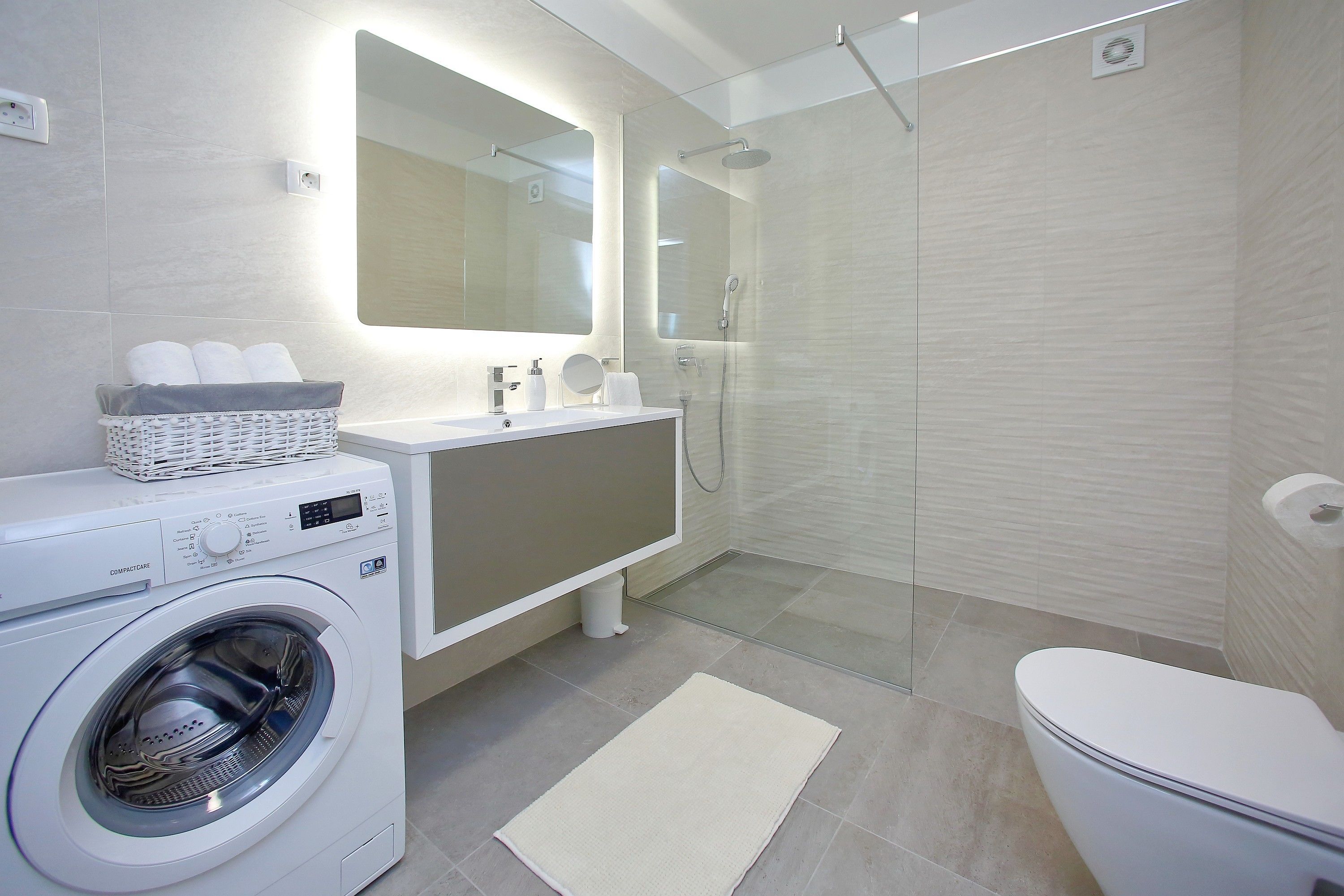 A modern bathroom with a washing machine, a sink, a mirror, and a shower.
